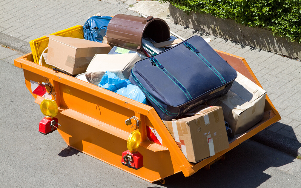 Riesiger orangener Container mit verschiedenen Gegenständen wie Kartons, Koffer & Müllbeutel und -tonnen