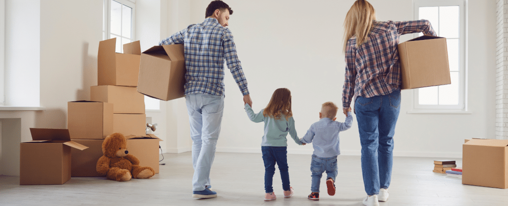 Eine Familie mit 2 kleinen Kindern läuft mit Umzugskartons durch die Wohnung