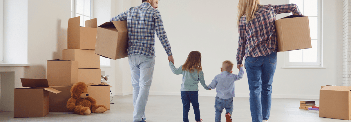 Eine Familie mit 2 kleinen Kindern läuft mit Umzugskartons durch die Wohnung